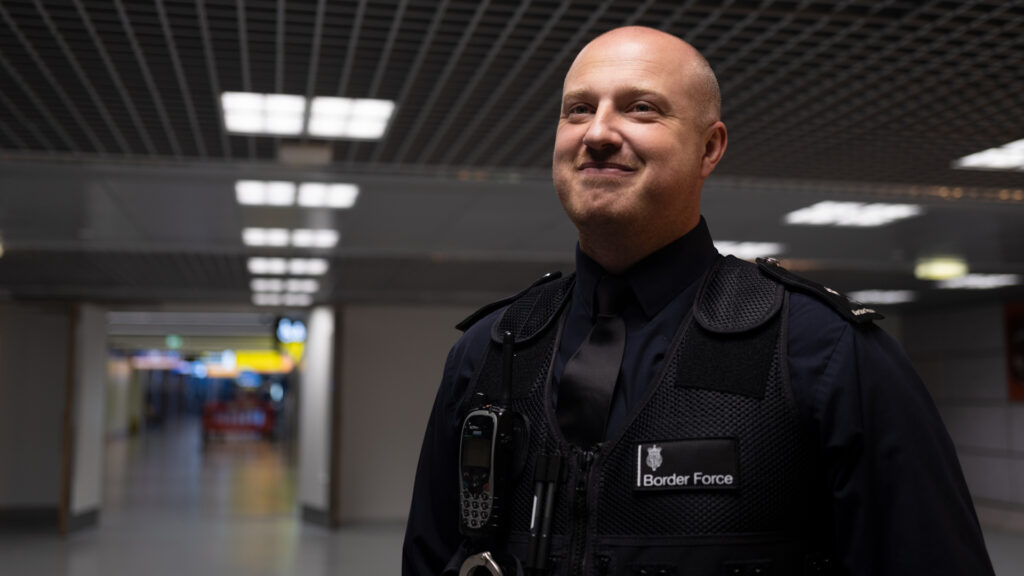 Uniformed Border Force Officer standing against the backdrop of an airport.