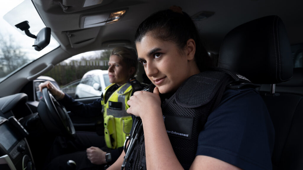 Two female Immigration Enforcement officers driving in a car