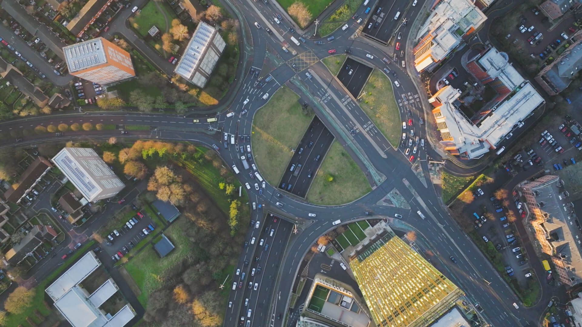 Aerial view of a large multi-lane roundabout with heavy traffic surrounded by buildings and green spaces.