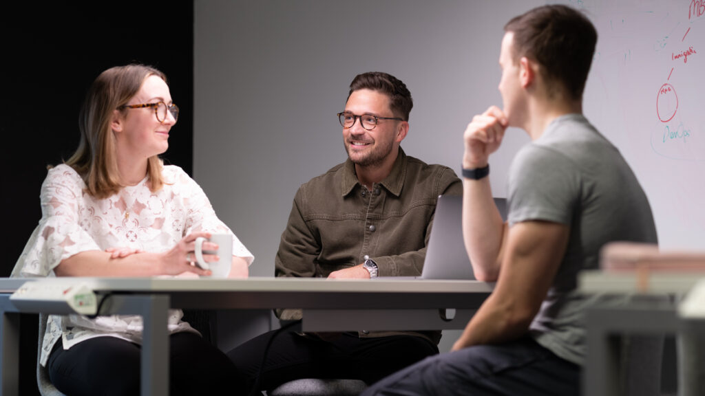 three members of staff seated around desk in meeting room