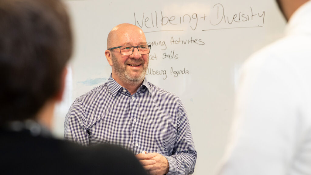 A male standing in front of an office white board presenting