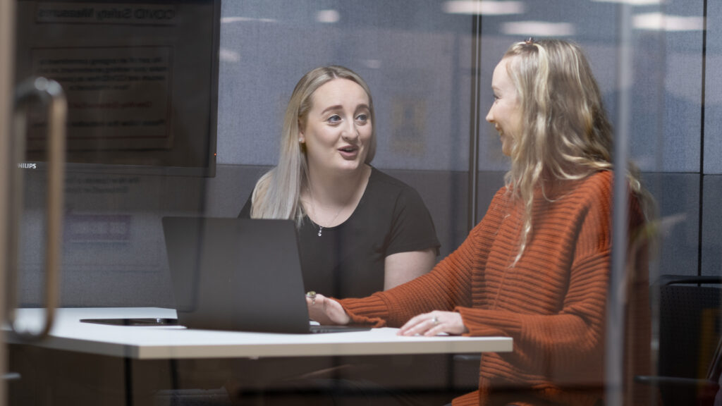 Two members of staff seated looking at a laptop
