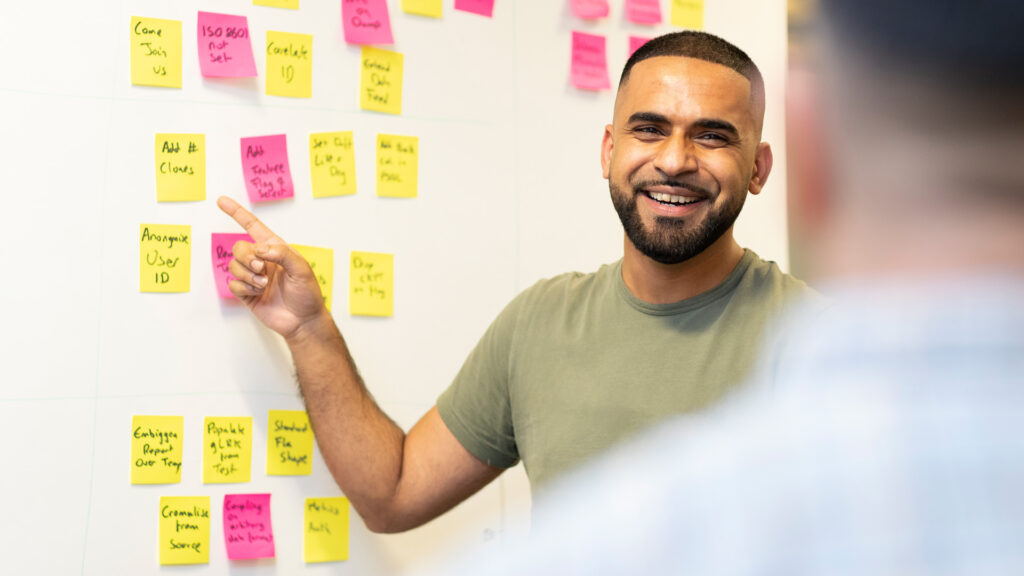 member of staff pointing to white board with post it notes on