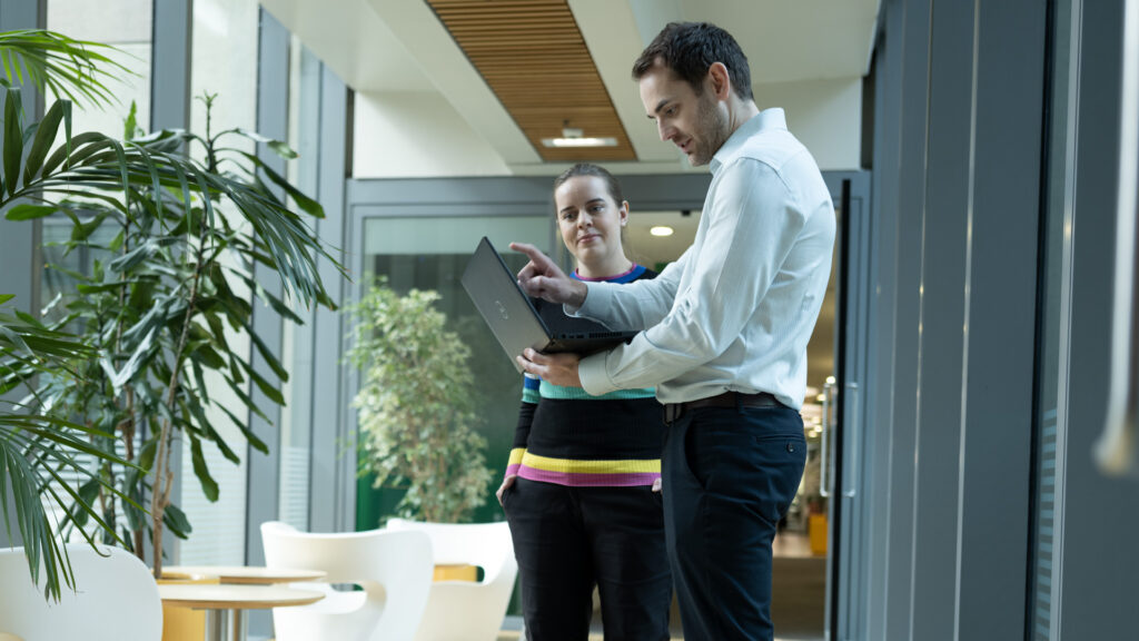 two members of staff standing looking at a laptop