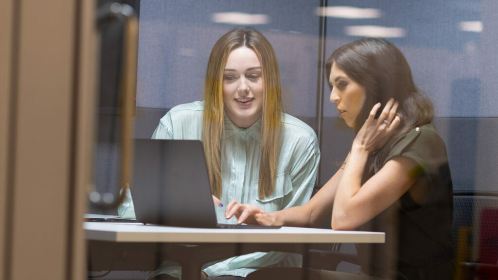Two members of staff seated looking at laptop