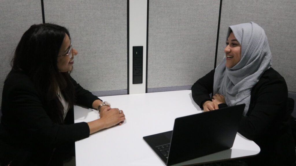 Two members of staff sitting opposite each other with laptop on desk