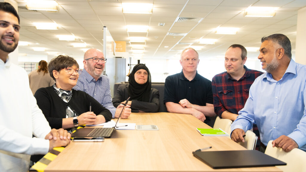 Seven members of staff standing around desk with laptop