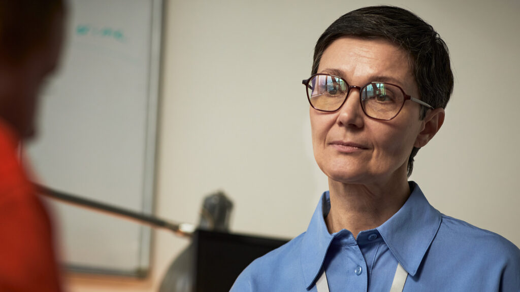 Person with glasses speaking with someone just off camera