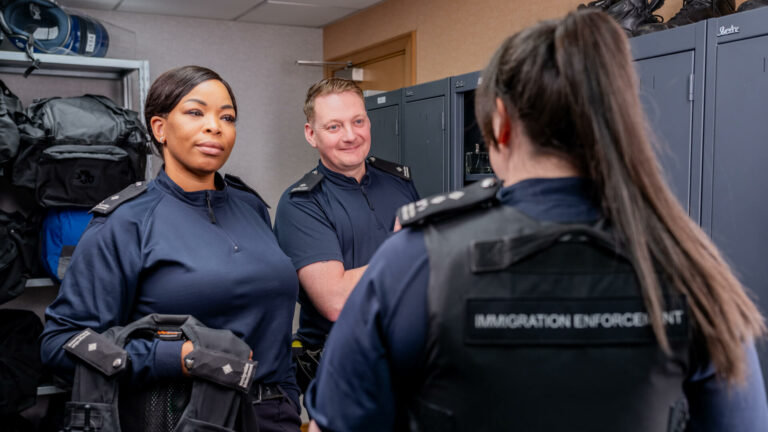 Three Immigration Enforcement Officers stood in a locker room.