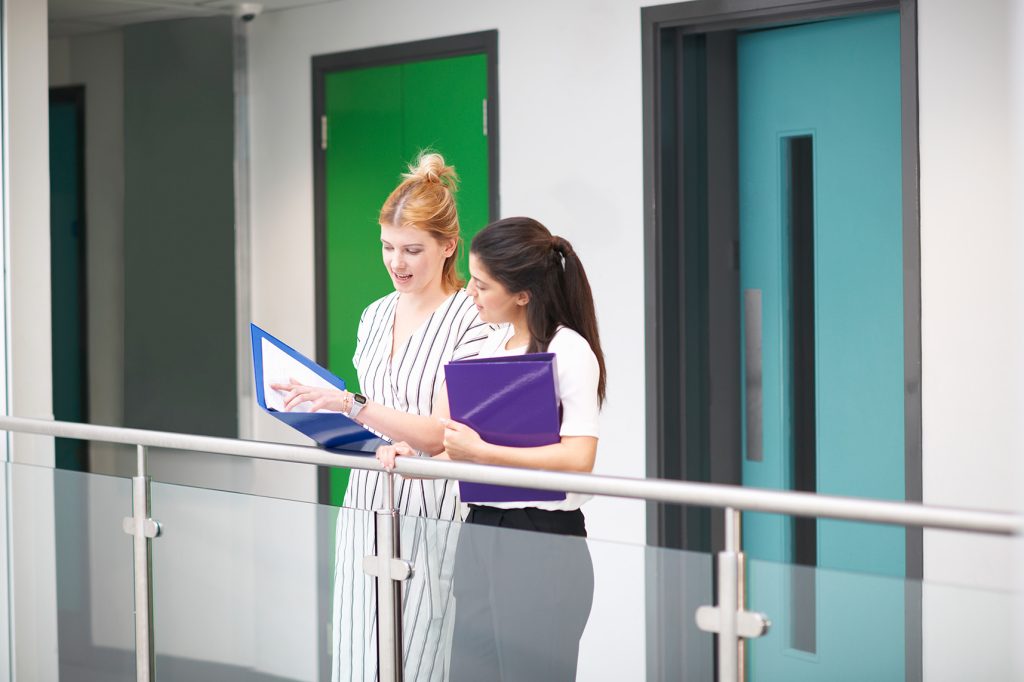 Two colleagues, on an office balcony looking into a folder
